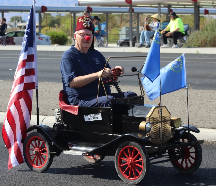 Pahrump Fall Festival Parade & Car Show - image of Shriners Hospital for Children Las Vegas Zelzah Flivvers member driving a battery powered replica car with flags.