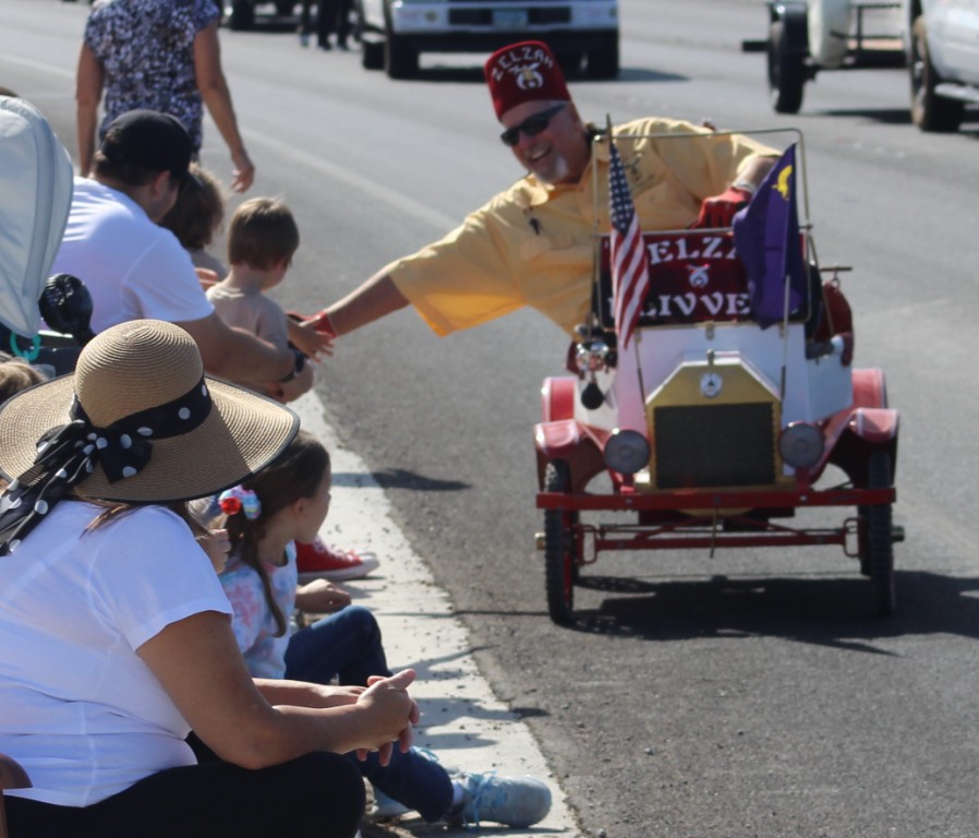 Pahrump Fall Festival Parade & Car Show - image of Shriners Hospital for Children Las Vegas Zelzah Flivvers member driving a battery powered replica car shaking hands with parade audience.