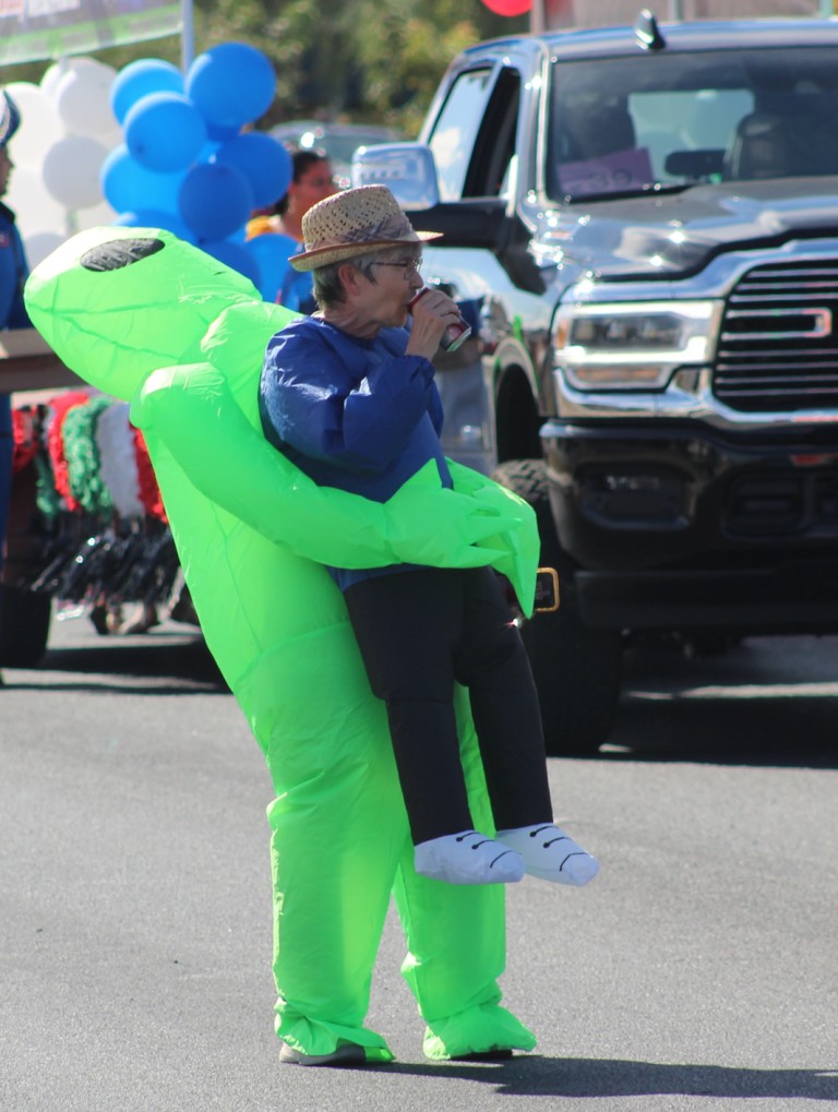 Pahrump Fall Festival Parade & Car Show - image of older woman wearing an inflatable alien body suit drinking soda.
