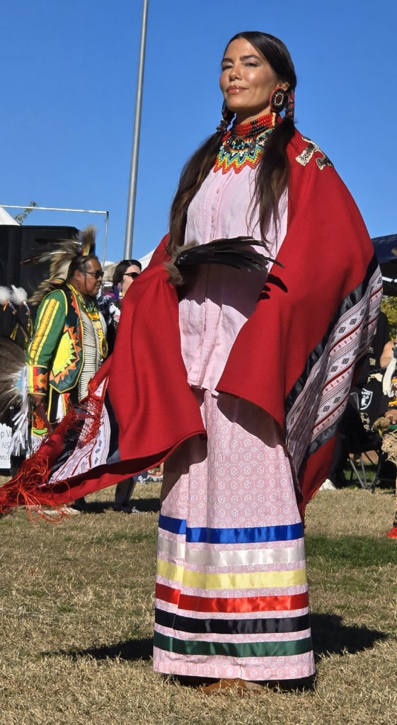 Image of a regal Native American female dressed in a colorful shawl holding her Eagle Feather fan as seen in powwows: Cedar Band; Cedar City; Duck Valley; Elko; Ely; Fallon; Fort Mojave; Goshute; Las Vegas; Snow Mountain; Las Vegas Snow Mountain; Las Vegas Paiute Tribe; Las Vegas Snow Mountain Paiute; Las Vegas Snow Mountain Paiute Tribe; 33rd annual Las Vegas Snow Mountain Paiute; Moapa; Muckleshoot; Nevada Day; Numaga; Pahrump; Pahrump Valley; Pahrump Valley Social; Pahrump Social; Petrack; Petrack Park; Red Dress; Sacred Visions; San Marcos; San Marcos Apache; Stewart; Sycuan; UNLV; UNR; Univ. of Nev. Reno; and Walker River; & Western Navajo Fair.